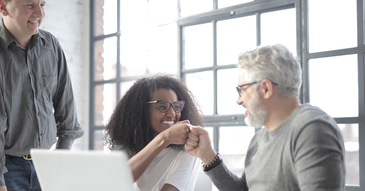 Freelance writer and happy client bumping fists near computer in office